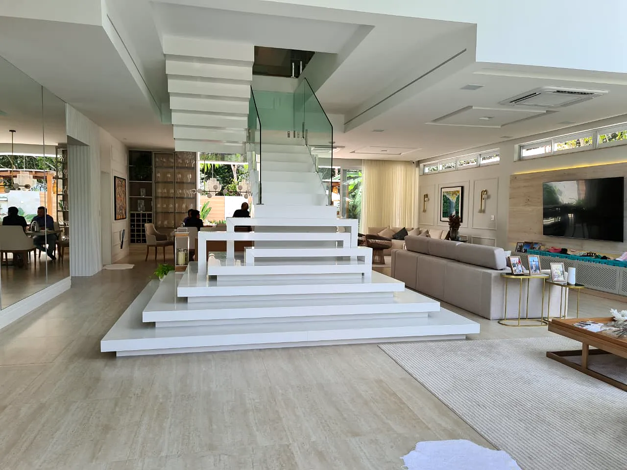 Escada escultural em branco com guarda-corpo de vidro, em sala integrada de residência.